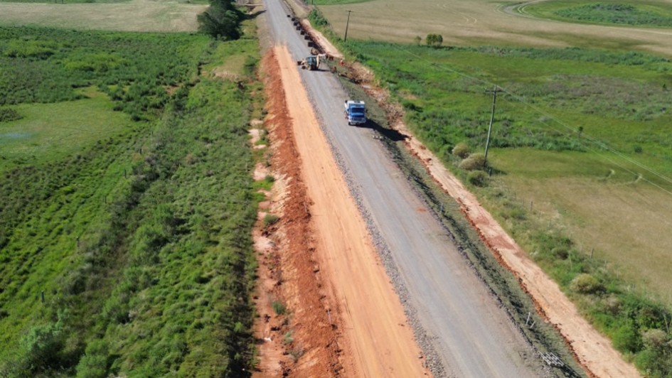 Foto aérea de uma estrada simples, de mão dupla, em meio à vegetação baixa.