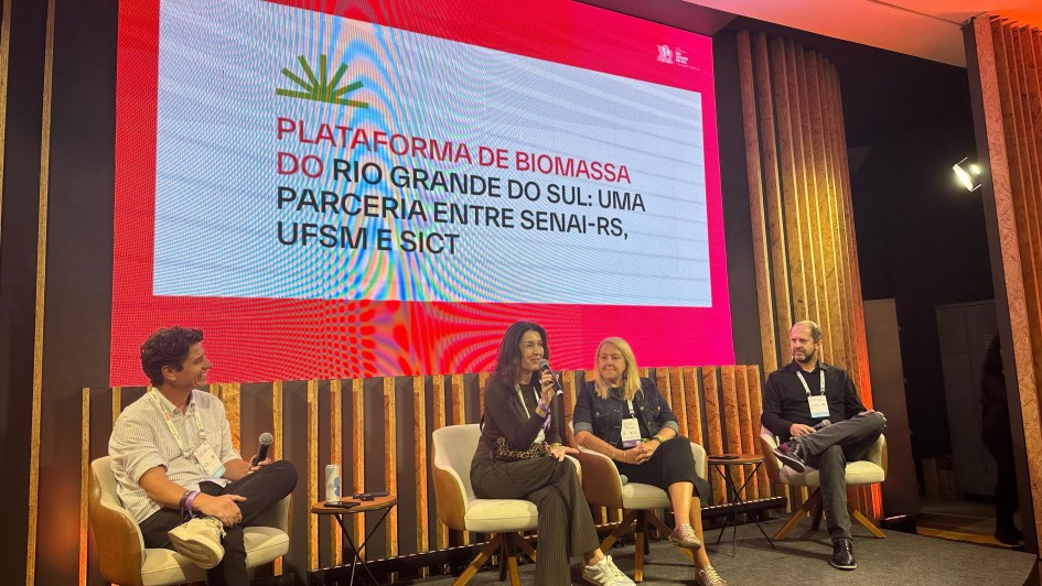 A imagem mostra quatro palestrantes (duas mulheres e dois homens) sentados em um palco, diante de um painel nas cores branca e rosa. No painel está escrito: "Plataforma de biomassa do Rio Grande do Sul: uma parceria entre Senai-RS, UFSM e Sict".