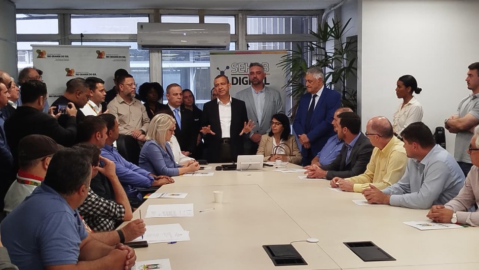Foto mostra reunião de representantes municipais na Secretaria de Habitação e Regularização Fundiária, tendo ao centro o secretário Carlos Gomes.