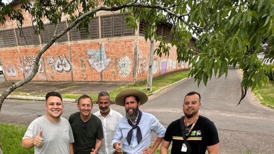 Foto mostra equipe da SEL e da Prefeitura de Novo Hamburgo posando para foto na praça, debaixo de uma árvore e em frente a um ginásio.
