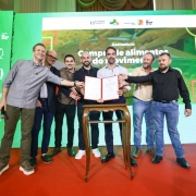 Foto mostra governador Eduardo Leite com documento em m&atilde;os, tendo pessoas ao seu lado, no ato do Pal&aacute;cio Piratini