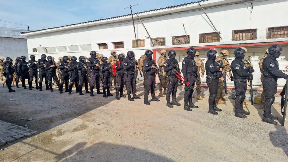 Foto mostra agentes penais enfileirados diante do muro de uma unidade prisional