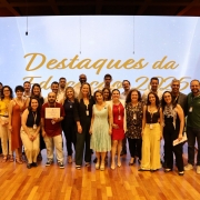 Foto mostra grupo de pessoas com certificados e posando juntas para fotos, em frente a um tel&atilde;o com a palavra "Destaques".