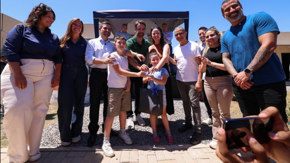 Foto posada em ambiente aberto, onde Leite aparece ao centro, de p&eacute;, com cinco pessoas tamb&eacute;m de p&eacute; enfileiradas de cada lado. Leite entrega uma chave para duas crian&ccedil;as.