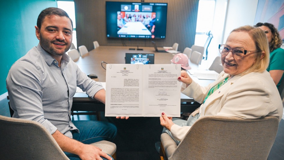 Vice governador Gabriel Souza aparece na foto ao lado da secret&aacute;ria Arita Bergmann, ambos seguram um documento, com uma tela com outros participantes online ao fundo.