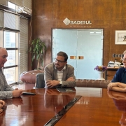 A imagem mostra tr&ecirc;s homens sentados em torno de uma mesa de reuni&atilde;o, conversando. Ao fundo, se l&ecirc; "Badesul". 