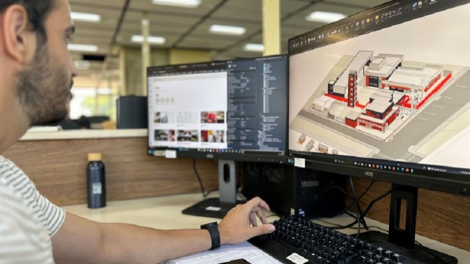 A imagem mostra um homem olhando para dois monitores em sua mesa de trabalho. Na tela, aparecem projetos de obras.  