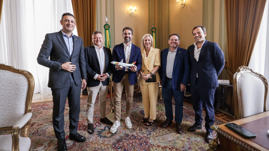 Foto do governador Eduardo Leite com comitiva da TAP. Todos est&atilde;o posando para foto. Governador segura uma miniatura de um avi&atilde;o.