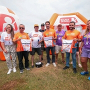 Aqui est&aacute; a descri&ccedil;&atilde;o detalhada da imagem para fins de acessibilidade:

A imagem registra um evento institucional realizado em um gramado ao ar livre sob c&eacute;u nublado, com a presen&ccedil;a de autoridades do governo do Rio Grande do Sul.

Figuras Centrais e A&ccedil;&atilde;o: No centro da composi&ccedil;&atilde;o, um grupo de oito pessoas posa para a foto. O governador Eduardo Leite e o vice-governador Gabriel Souza, acompanhados de um terceiro homem, seguram &agrave; frente do corpo mochilas do tipo saco de cor branca. Nas mochilas, l&ecirc;-se em destaque a frase: "Na estrada, o salva-vidas &eacute; voc&ecirc;.".

Vestimentas e Identidade Visual: * Eduardo Leite e Gabriel Souza vestem camisetas laranjas com o logotipo da campanha "Ver&atilde;o Total".

Outros integrantes do grupo usam camisetas roxas, tamb&eacute;m com a marca do "Ver&atilde;o Total", ou camisetas brancas com o logo da "Balada Segura".

Elementos de Fundo: * &Agrave; esquerda, h&aacute; um grande infl&aacute;vel em formato esf&eacute;rico (semelhante a um capacete ou bal&atilde;o), nas cores laranja e branco, exibindo a marca "BALADA SEGURA" e o &iacute;cone de uma pessoa com cinto de seguran&ccedil;a.

Ao fundo, uma estrutura infl&aacute;vel laranja em formato de tenda tamb&eacute;m exibe o logotipo da "Balada Segura".

Uma parte de um ve&iacute;culo branco &eacute; vis&iacute;vel na extremidade esquerda da foto.