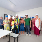 A imagem registra uma cerim&ocirc;nia de inaugura&ccedil;&atilde;o em um ambiente interno, focada no momento do corte da fita.

A&ccedil;&atilde;o Central: No centro da composi&ccedil;&atilde;o, um homem e uma mulher cortam uma fita verde.

O homem, &agrave; esquerda, usa &oacute;culos e terno escuro.

A mulher, &agrave; direita, tem cabelos curtos, usa &oacute;culos, blazer branco, blusa escura e cal&ccedil;a verde clara. Ambos sorriem durante o ato.

Acompanhantes: &Agrave; direita da mulher, uma pessoa de blusa azul-petr&oacute;leo aplaude a a&ccedil;&atilde;o. &Agrave; extrema esquerda, em primeiro plano, um senhor de camisa azul clara e &oacute;culos observa o corte da fita.

O Cen&aacute;rio: O evento ocorre em frente a uma porta branca de correr, onde est&aacute; aplicado o logotipo do "Assistir - Programa de Incentivos Hospitalares". O logo apresenta o desenho estilizado de um hospital com uma cruz vermelha ao centro.

Detalhes do Ambiente: Na parede lateral, de cor azul, h&aacute; quadros ou cartazes com fotografias de autoridades e textos informativos. O piso &eacute; de azulejos claros com um padr&atilde;o de c&iacute;rculos repetitivos.

Ilumina&ccedil;&atilde;o e Clima: A luz &eacute; clara e uniforme, t&iacute;pica de ambientes internos institucionais, e o clima &eacute; de formalidade e celebra&ccedil;&atilde;o.