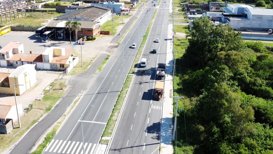 Foto a&eacute;rea de uma estrada duplicada de m&atilde;o dupla. Alguns carros passam por ela. &Agrave; direita, h&aacute; uma mata.