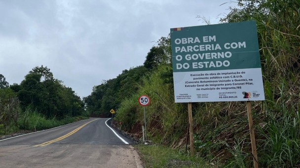A imagem mostra um obra de pavimenta&ccedil;&atilde;o asf&aacute;ltica. No lado direito da foto, h&aacute; uma placa onde se l&ecirc; "Obra em parceria com o governo do Estado". 