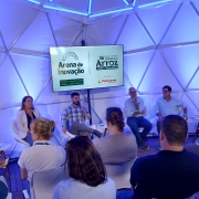 Esta &eacute; a descri&ccedil;&atilde;o detalhada da sexta imagem para fins de acessibilidade:

Imagem 6: Painel na Arena de Inova&ccedil;&atilde;o
A imagem registra uma palestra ou painel de discuss&atilde;o ocorrendo dentro de uma estrutura moderna durante um evento agr&iacute;cola.

Cen&aacute;rio e Ambiente:

A atividade acontece dentro de um domo geod&eacute;sico, com uma estrutura interna composta por tri&acirc;ngulos met&aacute;licos aparentes.

O ambiente &eacute; banhado por uma ilumina&ccedil;&atilde;o azulada tecnol&oacute;gica.

O piso &eacute; de deque de madeira clara.

Painelistas:

Cinco pessoas (duas mulheres e tr&ecirc;s homens) est&atilde;o sentadas em cadeiras brancas de design moderno, dispostas em semic&iacute;rculo.

Ao centro, um homem de camisa xadrez fala ao microfone. Os demais membros do painel ouvem atentamente ou consultam documentos.

Elementos Visuais e Informativos:

Tela Central: Um grande monitor exibe as marcas do evento: "Arena de Inova&ccedil;&atilde;o" e "36&ordf; Abertura Oficial da Colheita do Arroz". O texto na tela indica a data de 24 a 26 de fevereiro de 2026, em Embrapa - Cap&atilde;o do Le&atilde;o - RS.

Tela Lateral: &Agrave; direita, um monitor menor exibe a mensagem "FA&Ccedil;A SUA PERGUNTA" junto a um QR Code e um n&uacute;mero de WhatsApp para intera&ccedil;&atilde;o do p&uacute;blico.

P&uacute;blico: No primeiro plano, vemos as costas e cabe&ccedil;as de alguns espectadores sentados, focados na apresenta&ccedil;&atilde;o.