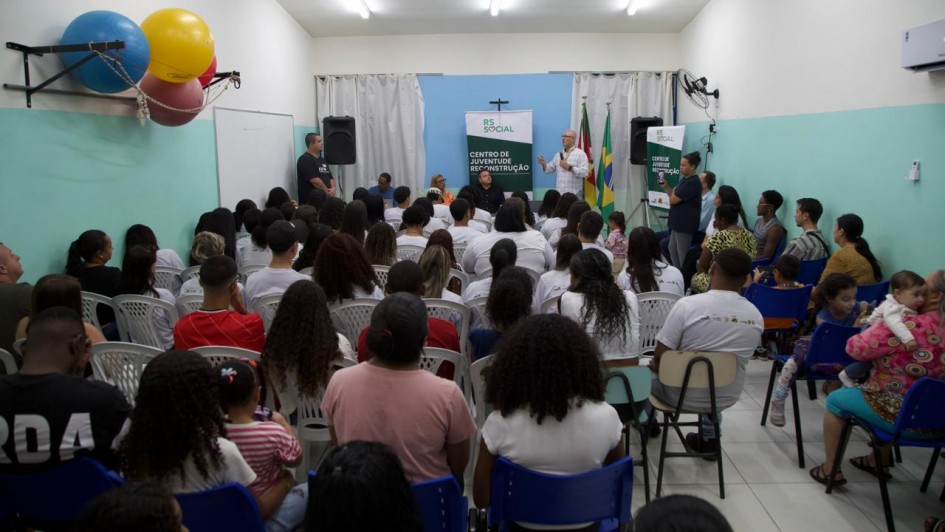 Foto mostra uma sala cheia de pessoas sentadas que acompanham um palestrante que est&aacute; de p&eacute; com um microfone. 