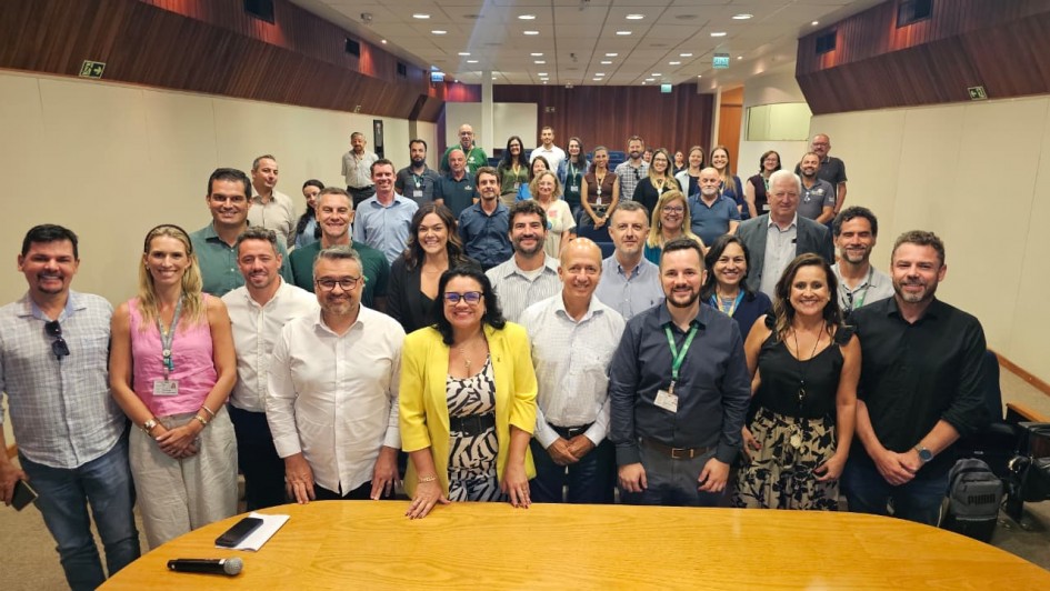 Foto posada num audit&oacute;rio. &Agrave; frente, h&aacute; uma mesa. Atr&aacute;s dela, at&eacute; o fundo do audit&oacute;rio aparecem mais de 50 pessoas de p&eacute;, que olham para a c&acirc;mera. Boa parte sorri.