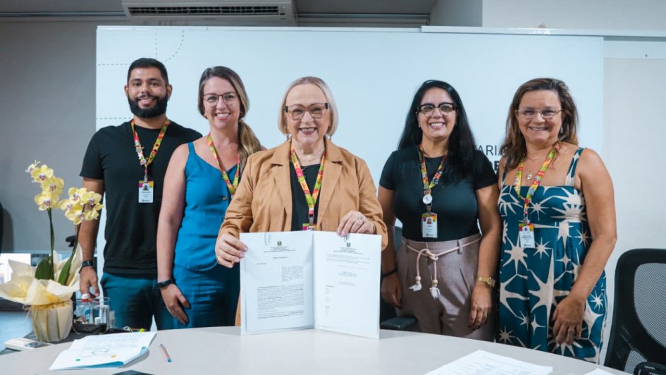 Foto mostra a secret&aacute;ria da Sa&uacute;de, Arita Bergmann, posando para foto com outros quatro servidores. Ela segura um documento assinado.