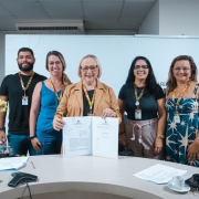 Foto mostra a secret&aacute;ria da Sa&uacute;de, Arita Bergmann, posando para foto com outros quatro servidores. Ela segura um documento assinado.