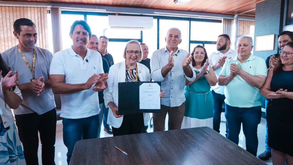 Foto mostra secret&aacute;ria Arita Bergmann segurando um documento. Outras pessoas est&atilde;o na volta e aplaudem o ato.