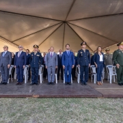 A foto mostra uma fileira de autoridades e integrantes do Corpo de Bombeiros posicionados em p&eacute; sobre um palco elevado. Algumas pessoas vestem uniformes militares escuros ou verdes, enquanto outras usam trajes sociais formais. 