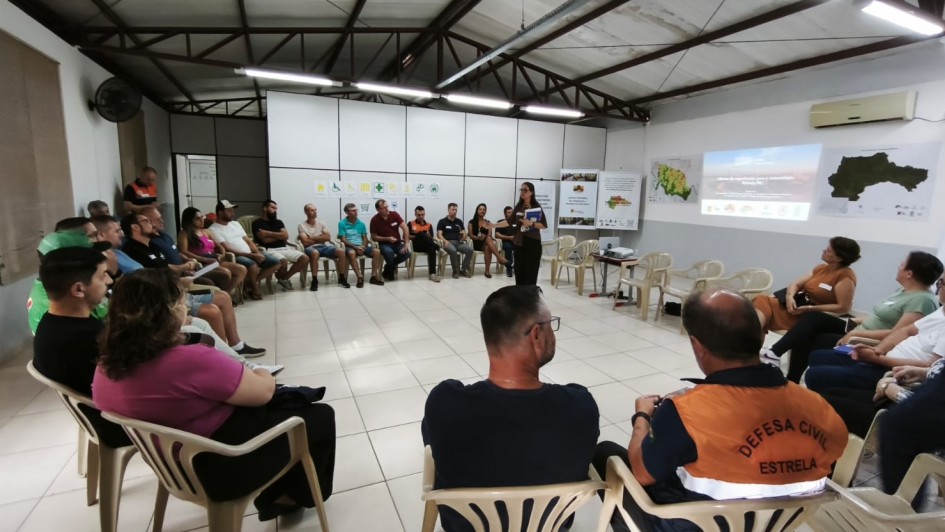 A foto mostra uma reuni&atilde;o em formato de roda de cadeiras dentro de uma sala ampla. As pessoas est&atilde;o organizadas em c&iacute;rculo, assistindo a uma apresenta&ccedil;&atilde;o feita por uma pessoa posicionada ao centro. 