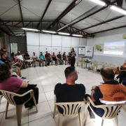 A foto mostra uma reuni&atilde;o em formato de roda de cadeiras dentro de uma sala ampla. As pessoas est&atilde;o organizadas em c&iacute;rculo, assistindo a uma apresenta&ccedil;&atilde;o feita por uma pessoa posicionada ao centro. 