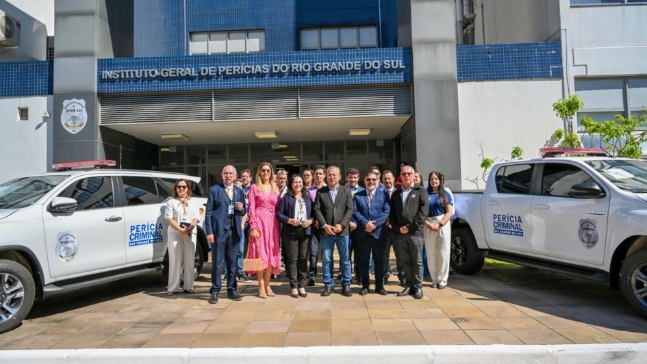 Secret&aacute;rio Ikeda e servidores do IGP posam para fotografia entre duas viaturas novas. Ao fundo, a fachada do pr&eacute;dio do IGP.