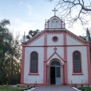 Imagem mostra a fachada do Santuário de Caaró, em Caibaté. Uma igreja branca, com colunas e detalhes em rosa. No topo, um arco sustenta um crucifixo.