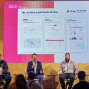 Esta &eacute; uma descri&ccedil;&atilde;o detalhada da imagem para fins de acessibilidade:

A fotografia registra um painel t&eacute;cnico durante o South Summit Brazil 2026, em Porto Alegre, focado em seguran&ccedil;a p&uacute;blica e inova&ccedil;&atilde;o de dados.

O Palco e os Participantes
Os Palestrantes: Tr&ecirc;s homens est&atilde;o sentados em poltronas de design moderno sobre um palco.

Ao centro: Ant&ocirc;nio Padilha, um homem de cabelos escuros e barba curta, veste um terno azul e fala ao microfone. Ele gesticula com a m&atilde;o esquerda enquanto explica o conte&uacute;do da tela.

&Agrave; esquerda: Um homem de barba e &oacute;culos, vestindo um blazer escuro sobre camiseta preta, observa a plateia.

&Agrave; direita: Um homem com uma barba longa e volumosa, vestindo uma camisa cinza de mangas compridas, segura um microfone e ouve atentamente. Todos utilizam os crach&aacute;s verdes oficiais do evento.

Mobili&aacute;rio: O palco &eacute; revestido com placas de madeira compensada (OSB), e ao lado de cada poltrona h&aacute; pequenas mesas de apoio pretas.

Conte&uacute;do da Tela (Apresenta&ccedil;&atilde;o)
Ao fundo, um grande tel&atilde;o de LED exibe uma apresenta&ccedil;&atilde;o intitulada "Do territ&oacute;rio &agrave; prioriza&ccedil;&atilde;o da a&ccedil;&atilde;o - Seguran&ccedil;a p&uacute;blica orientada por dados".

Infogr&aacute;ficos: A tela mostra tr&ecirc;s etapas l&oacute;gicas:

Territ&oacute;rio Cr&iacute;tico: Mapas com manchas de calor que identificam &aacute;reas de alta densidade criminal.

Prioriza&ccedil;&atilde;o: Gr&aacute;ficos de radar e tabelas para an&aacute;lise de anomalias.

Detalhamento: Gr&aacute;ficos de barras e mapas anal&iacute;ticos integrados.

Logotipos: No topo da tela, aparecem as marcas do South Summit, do programa RS SEGURO, do GESeg e o bras&atilde;o do Governo do Estado do Rio Grande do Sul.

Composi&ccedil;&atilde;o e P&uacute;blico
Primeiro Plano: Na parte inferior da foto, veem-se as silhuetas das cabe&ccedil;as de v&aacute;rias pessoas da plateia, sugerindo que o audit&oacute;rio est&aacute; cheio e atento.

Ilumina&ccedil;&atilde;o: A luz &eacute; quente e focada no palco, com o tel&atilde;o emitindo uma luz branca e rosada que preenche o ambiente. O cen&aacute;rio lateral possui ripas de madeira verticais que conferem profundidade &agrave; cena.

Atmosfera
A imagem transmite uma sensa&ccedil;&atilde;o de profissionalismo e avan&ccedil;o tecnol&oacute;gico. Ela exemplifica como o Estado utiliza intelig&ecirc;ncia de dados e transpar&ecirc;ncia para gerir a seguran&ccedil;a p&uacute;blica, apresentando esses resultados em um ambiente de inova&ccedil;&atilde;o global.