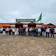 V&aacute;rias pessoas est&atilde;o em p&eacute; lado a lado para foto oficial, em ambos os lados, v&aacute;rios ve&iacute;culos estacionados e, ao fiundo, pavilh&atilde;o com uma bandeira do Brasil e a faixa com os dizeres Expoagro Afubra