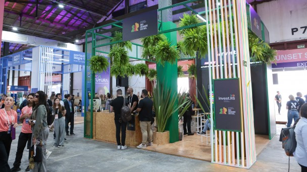 Foto mostra estande e pessoas circulando.