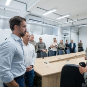 Amplo sagu&atilde;o com v&aacute;rias pessoas, civis e policiais militares. Em primeiro plano, dois homens vestidos de roupas civis conversam com dois homens vestidos de policiais militares, observados por um homem vestido com roupas civis