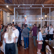 A fotografia mostra o interior do Museu das Missões com grande circulação de visitantes. Pessoas caminham e conversam em meio a painéis informativos e esculturas, enquanto a arquitetura do espaço combina elementos históricos com a expografia contemporânea, reforçando o diálogo entre memória, história e participação pública.

