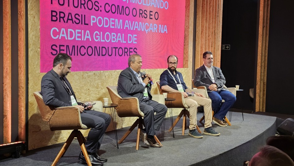 A imagem mostra um painel em um evento, com quatro pessoas sentadas em poltronas alinhadas no palco.