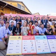Foto mostra governador Eduardo Leite e outras autoridades e participantes do South Summit reunidos para uma foto coletiva. Todos vibram e alguns fazem sinal de positivo com a m&atilde;o. Eles est&atilde;o na frente de uma placa com logomarcas do evento. A foto foi realizada na parte externa do cais Mau&aacute;, com parte dos armaz&eacute;ns aparecendo ao fundo.