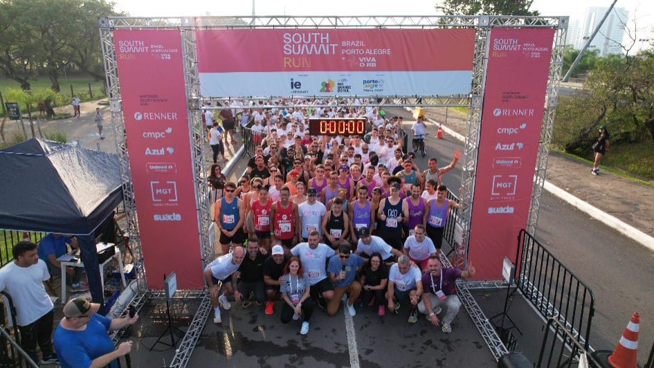 Imagem mostra v&aacute;rias pessoas paradas em um ponto de largada para uma corrida, com um &oacute;rtico, no qual consta a logomarca South Summit Run