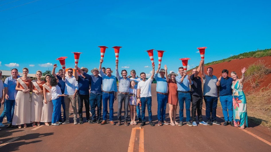 V&aacute;rias pessoas est&atilde;o lado a lado em uma estrada asfaltada com cones de tr&acirc;nsito levantados simbolizando a inaugura&ccedil;&atilde;o da estrada