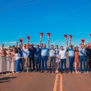 V&aacute;rias pessoas est&atilde;o lado a lado em uma estrada asfaltada com cones de tr&acirc;nsito levantados simbolizando a inaugura&ccedil;&atilde;o da estrada