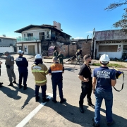 Um grupo de sete pessoas sob uma lona observa uma casa com avarias em sua fachada