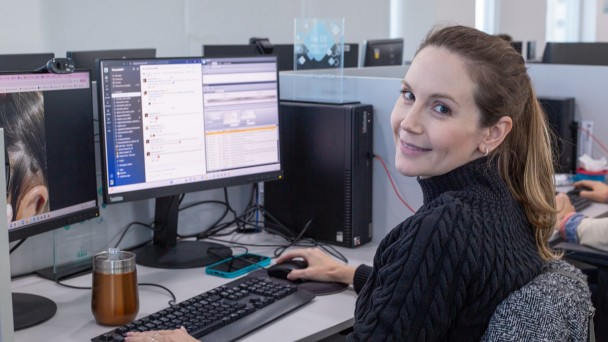 Foto mostra m&eacute;dica da Telessa&uacute;de atuando na &aacute;rea de dermatologia, ela est&aacute; sentada em frente ao computador e sorri para a c&acirc;mera.