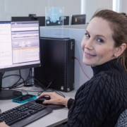 Foto mostra m&eacute;dica da Telessa&uacute;de atuando na &aacute;rea de dermatologia, ela est&aacute; sentada em frente ao computador e sorri para a c&acirc;mera.