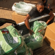 Foto mostra um servidor carregando uma carga em um ve&iacute;culo com itens do kit do M&atilde;e Ga&uacute;cha, com sacolas em verde claro e caixas de papel&atilde;o. 