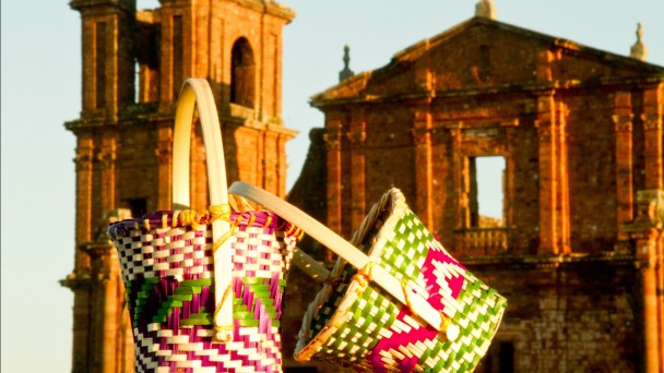 Foto mostra cestos com arte ind&iacute;gena em primeiro plano e ao fundo a fachada das ru&iacute;nas de S&atilde;o Miguel.