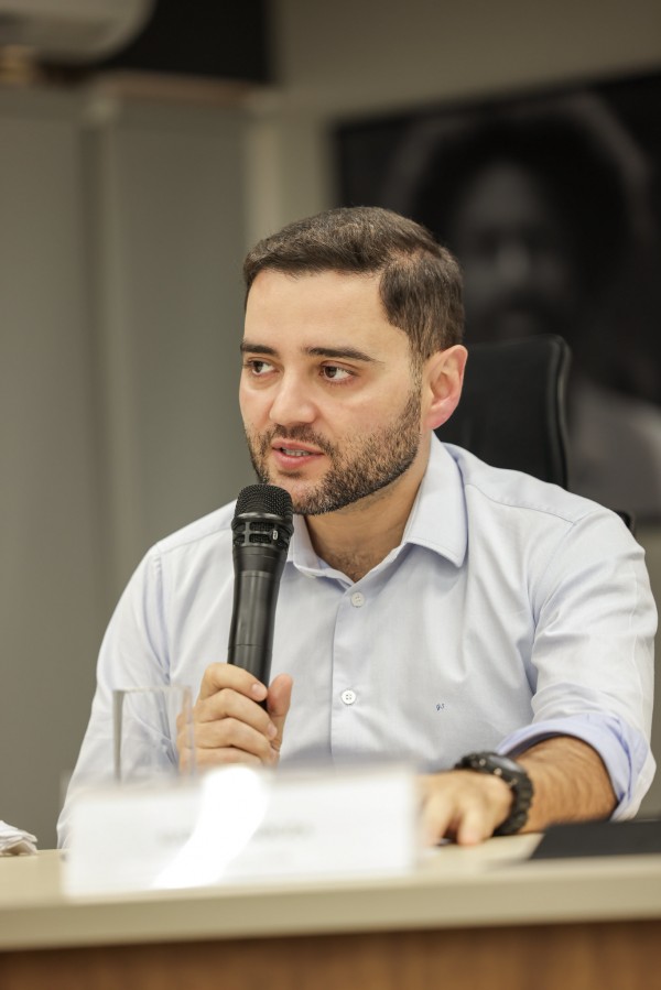 Foto mostra o vice-governador Gabriel Souza discursando sentado, segurando um microfone.