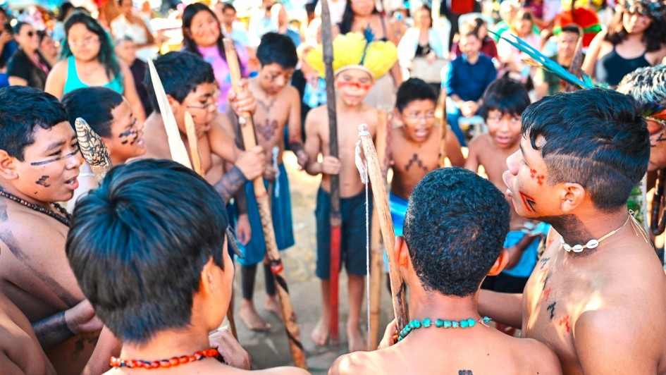 C&iacute;rculo de crian&ccedil;as e adolescentes ind&iacute;genas dan&ccedil;ando com pintura corporal e segurando objetos ind&iacute;genas durante a entrega da reforma na escola ind&iacute;gena Fag Nhin.