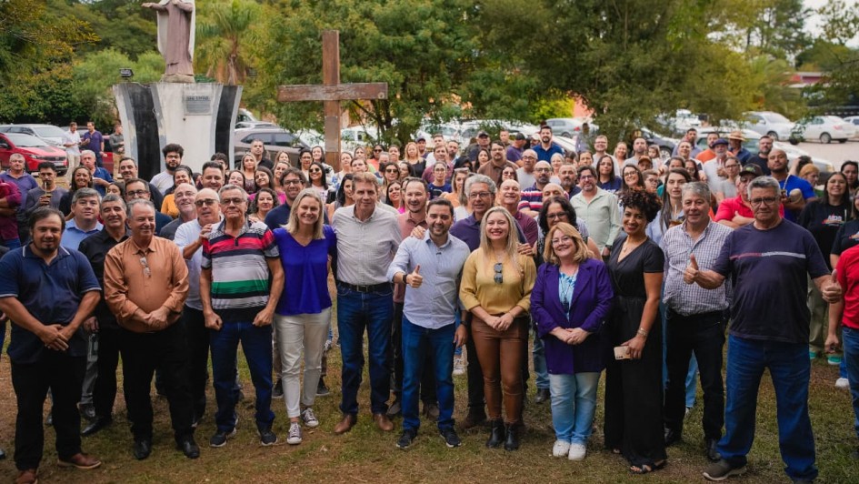 V&aacute;rias pessoas est&atilde;o paradas para foto, ao fundo monumentos religiosos como est&aacute;tua de uma santa e uma cruz
