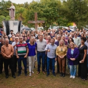 V&aacute;rias pessoas est&atilde;o paradas para foto, ao fundo monumentos religiosos como est&aacute;tua de uma santa e uma cruz