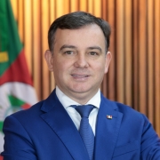 Homem de gravata e palet&oacute; azul pousa para foto oficial, &agrave; frente de uma bandeira do Rio Grande do Sul