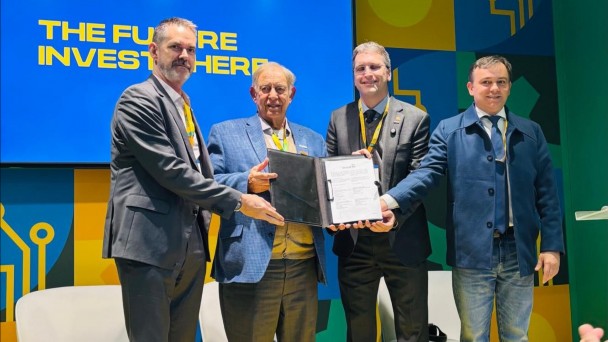 Foto mostra quatro homens segurando o documento assinado no palco da feira. 