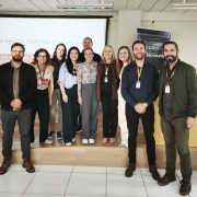A imagem mostra um grupo reunido em um ambiente interno de apresenta&ccedil;&otilde;es, organizado para registro coletivo em frente a uma tela de proje&ccedil;&atilde;o. No fundo, &eacute; poss&iacute;vel ler o texto &ldquo;Cluster Health Tech Rio Grande do Sul&rdquo;.