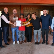 Registro coletivo em ambiente interno r&uacute;stico, com paredes de tijolo aparente e piso simples. Um grupo est&aacute; alinhado para foto, e ao centro um documento &eacute; exibido.